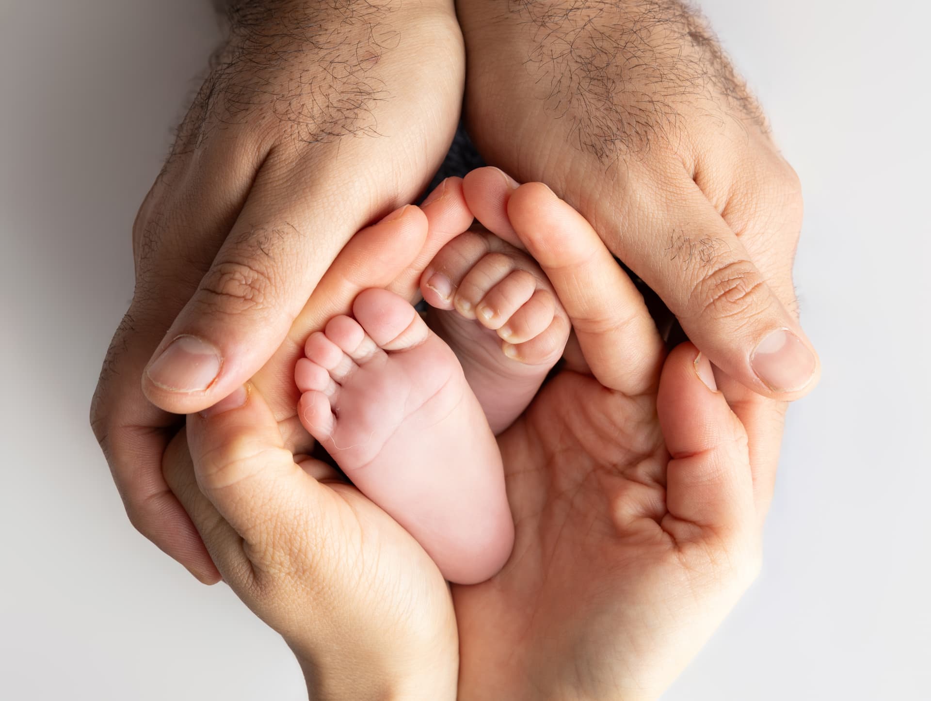 Newborn baby's tiny feet cradled in a parent's cupped hands against a soft white backdrop